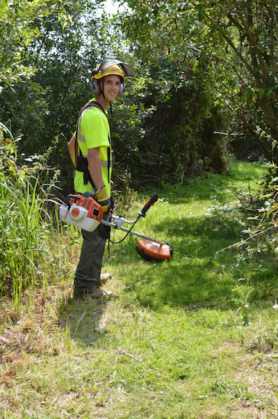 Growth Team member smiling at the camera with a strimmer